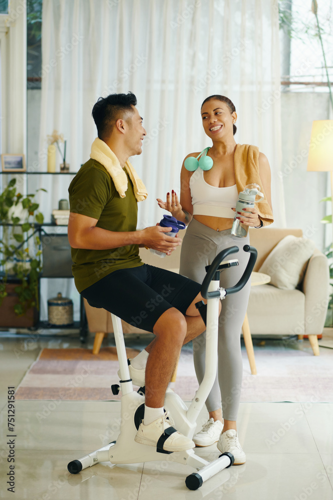 Sporty couple drinking water and chatting after working out together at home Sporty couple drinking water and chatting after working out together at home