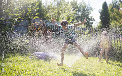 Summer holiday. Happy two kids siblings playing with garden hose and having fun with spray of water in sunny backyard. Summer time. 