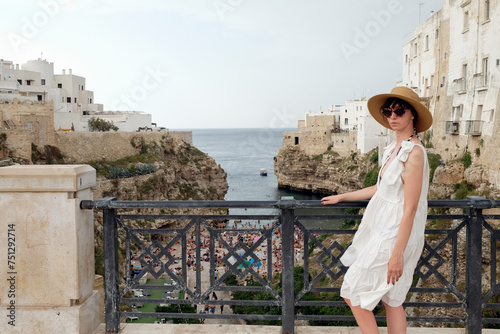 Female tourist with hat and sunglasses standing at Polignano A Mare
