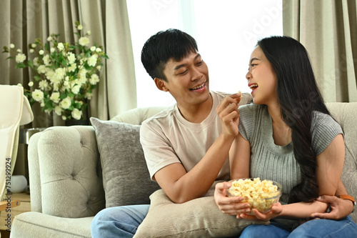 Cheerful young couple having fun while watching TV and eating popcorn at home. Leisure  entertainment and recreation concept