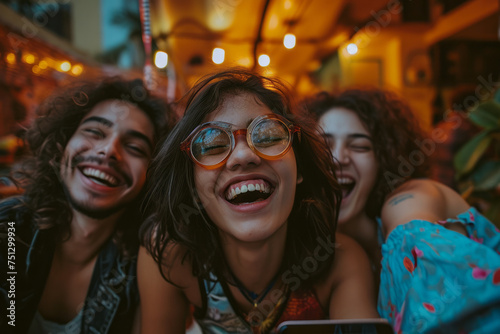A group of young adults gathered around, laughing together while focused on a cell phone screen © koala studio