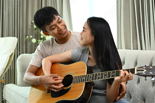Affectionate Asian couple playing guitar while relaxing on weekend at home