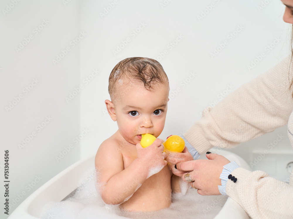 a boy playing in the bathtub with a rubber duck while his mother is bathing him a boy playing in the bathtub with a rubber duck while his mother is bathing him