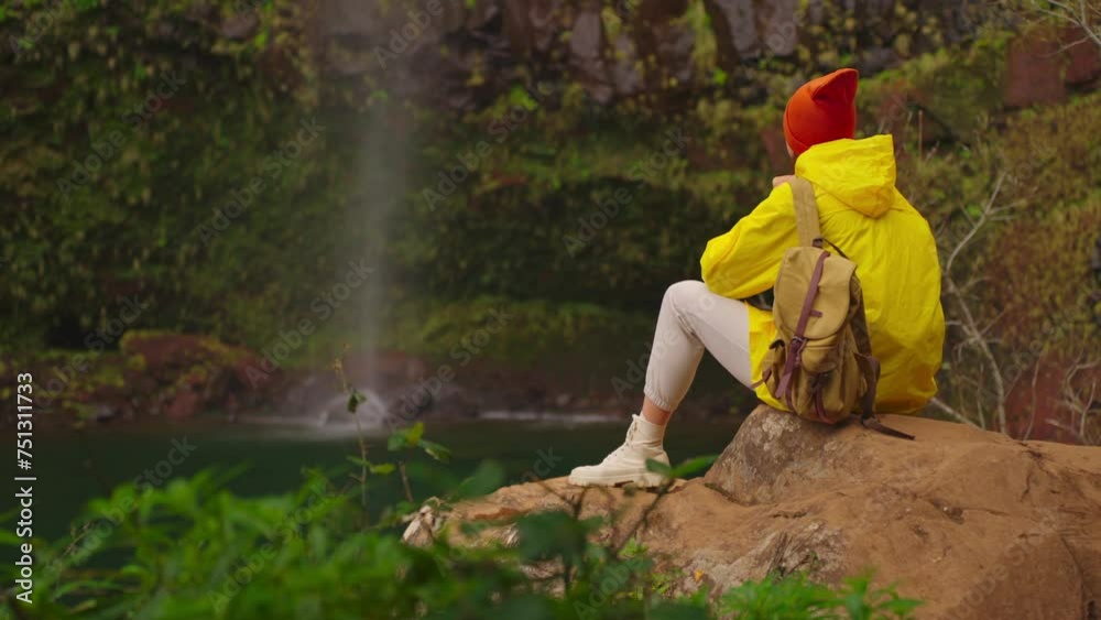 Woman traveler hiker in a yellow raincoat near waterfall in the highlands, enjoys nature and life. Traveling in the mountains, adventure in trip. Lifestyle concept. Traveller in yellow puffer jacket Woman traveler hiker in a yellow raincoat near waterfall in the highlands, enjoys nature and life. Traveling in the mountains, adventure in trip. Lifestyle concept. Traveller in yellow puffer jacket