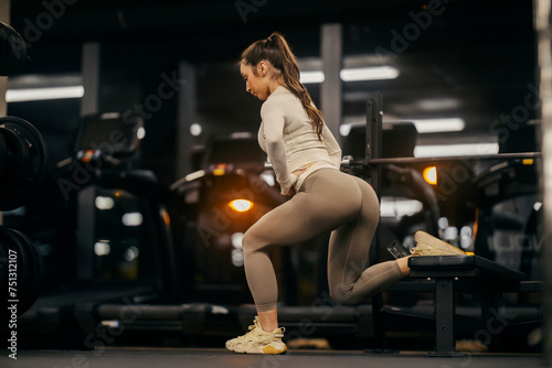 Side view of a fit sportswoman doing split squat workout on a bench in a gym.