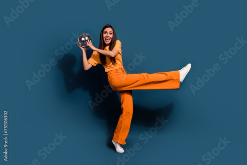 Full body length photo of crazy girl wear orange look seems happy with disco ball boogie woogie isolated on dark blue color background