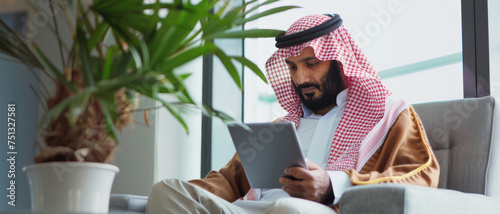 A man in traditional Arabic attire absorbed in his tablet.