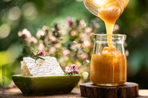 Pour honey into glass jar and honeycomb on natural background.