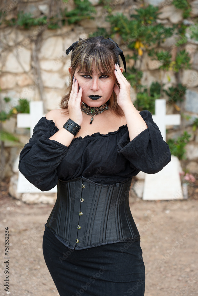 Victorian gothic woman wearing a black dress and a bustier that highlights her hips, posing thoughtfully next to graves in a cemetery in autumn full of jewels fallen to the ground	