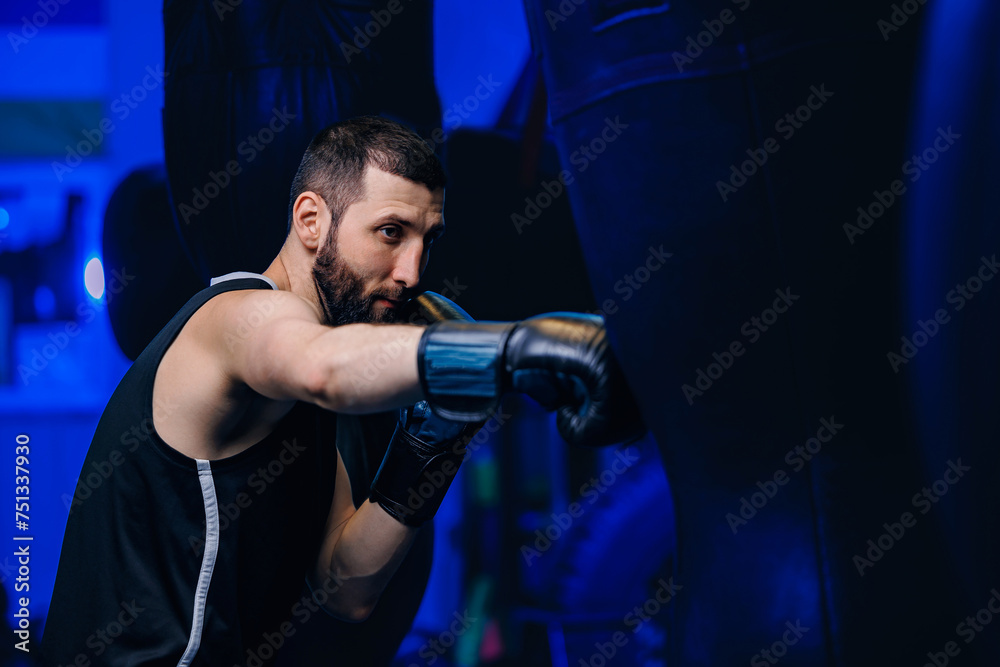 Male boxer trains punches on punching bag, dark background