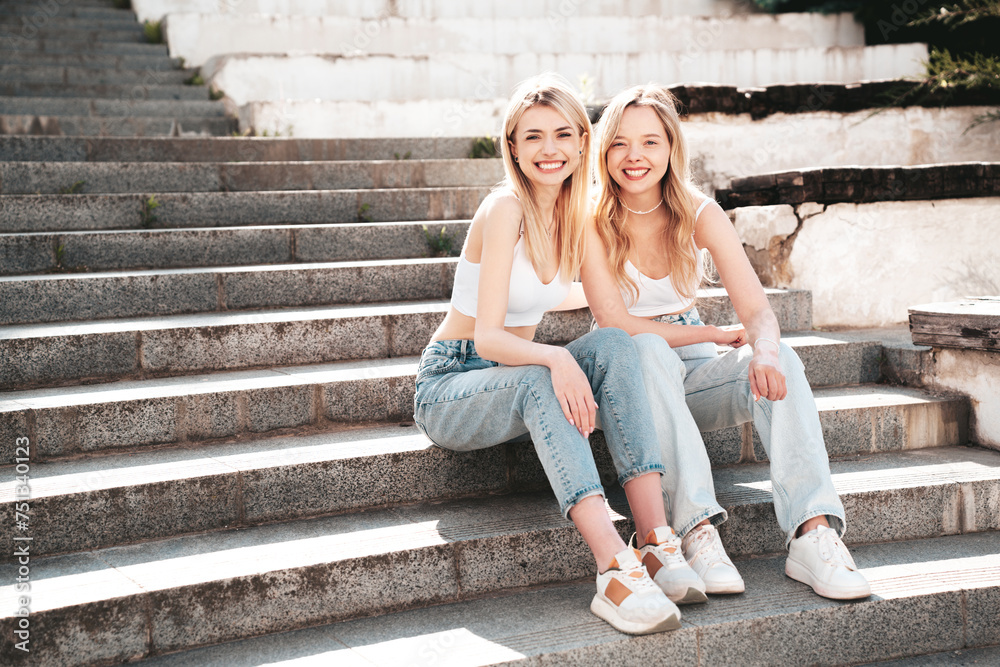 Two young beautiful smiling hipster female in trendy summer white top and jeans clothes. Carefree women posing in the street. Positive models having fun outdoors. Cheerful and happy
