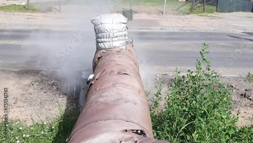 A damaged water pipeline with steam. A broken outdoor duct evaporates fog. Waterway line maintenance.