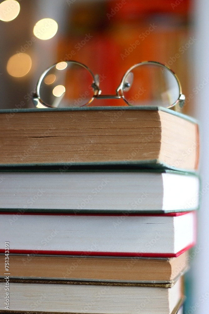 Stack of books, reading glasses and lit candles on the table. Rainbow bookshelf in the background. Selective focus.