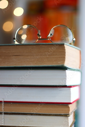 Obraz na płótnie Stack of books, reading glasses and lit candles on the table. Rainbow bookshelf in the background. Selective focus. w salonie