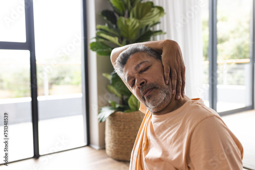 Biracial senior man with grey hair appears to have neck pain, wearing a casual orange shirt photo