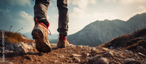 A hiker is seen carefully traversing rugged terrain  making their way up a hill on a bright and sunny day. The focus is on their feet as they take each step upwards.