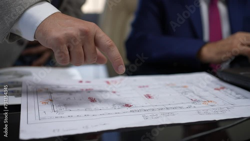 a human hand in a white collared suit pointing to certain areas with his hand on the project file. slow motion