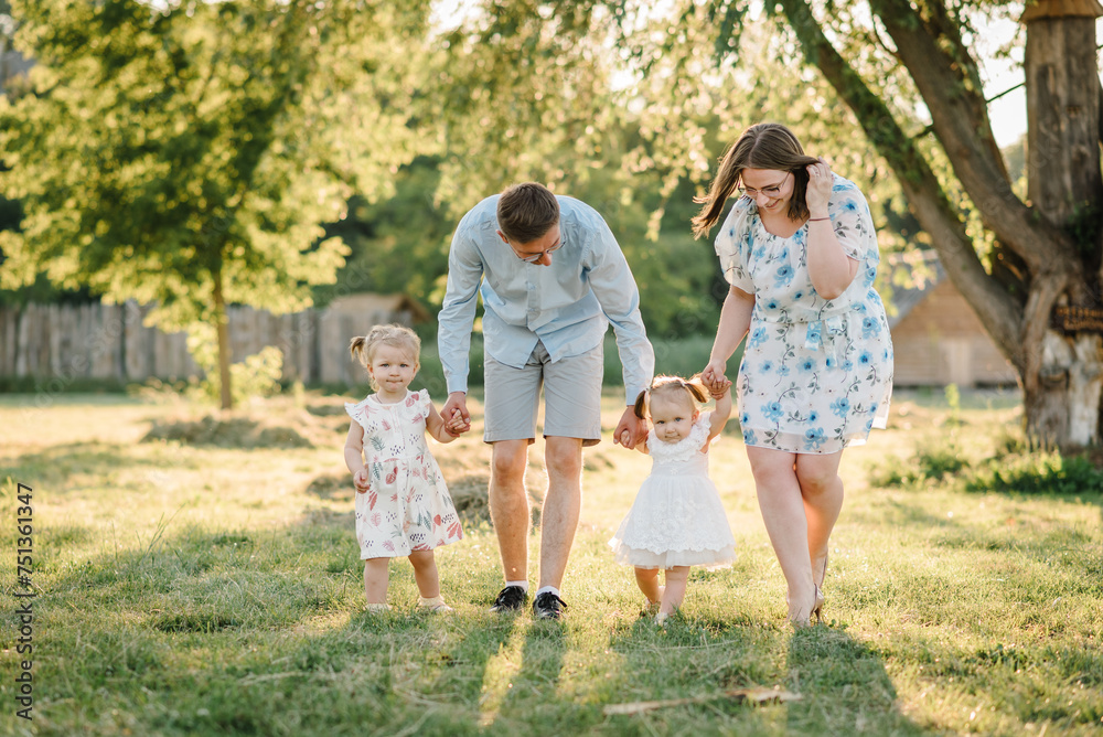 Mom, dad, and kids walking in park at sunset. Mother, father hold hands happy children daughter. Running in green grass in nature on summer day. Concept of family spending time together on a picnic.