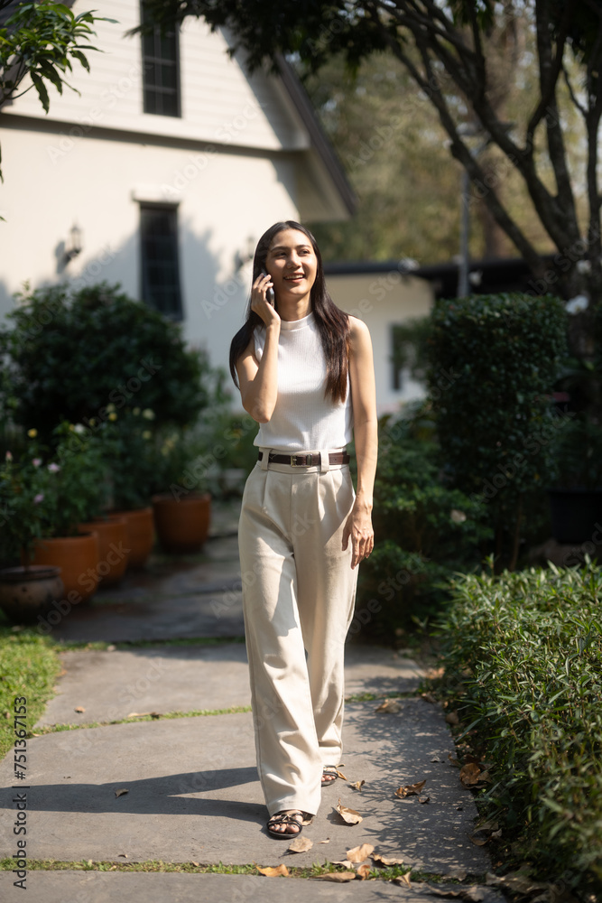 Cheerful young woman walks and talking on smartphone in lush green garden Cheerful young woman walks and talking on smartphone in lush green garden