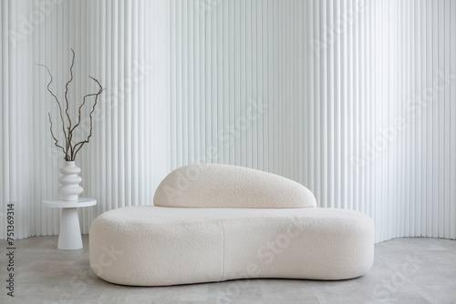 A cute soft white sofa against the backdrop of a foliated wall made of cylinders and a vase with dry branches