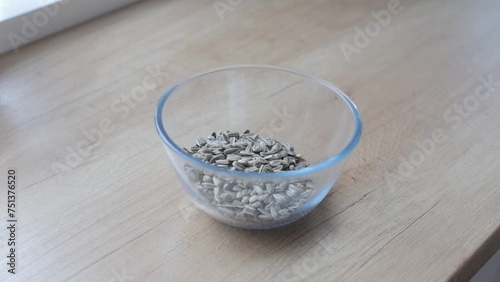 A woman's hand pours fried sunflower seeds from a transparent mug into a transparent bowl