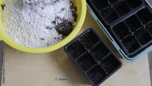 There is a container with soil and fertilizer on the table, and around there are containers for planting seedlings