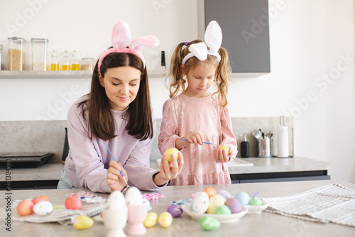 Smiling woman decorating Easter eggs wearing bunny headbands at home close up. Holiday season.