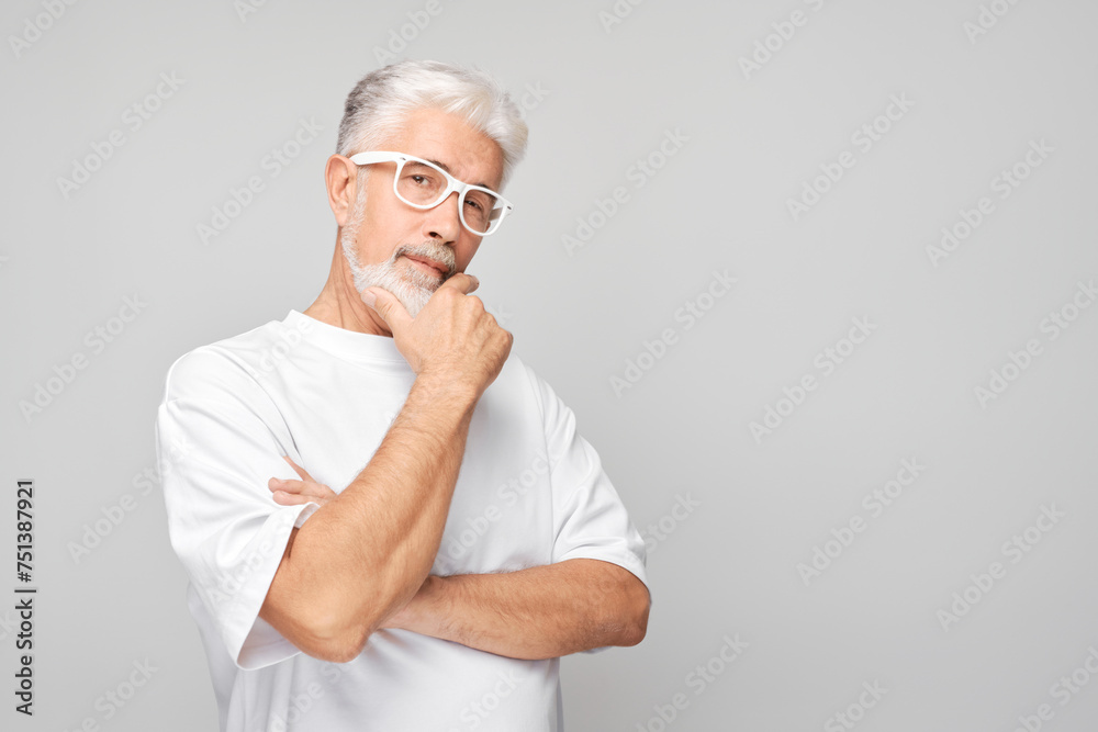 Mature man with white hair and glasses looking thoughtful against a gray background. Mature man with white hair and glasses looking thoughtful against a gray background.