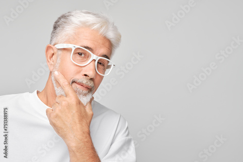 Mature man with white hair and glasses looking thoughtful against a gray background.