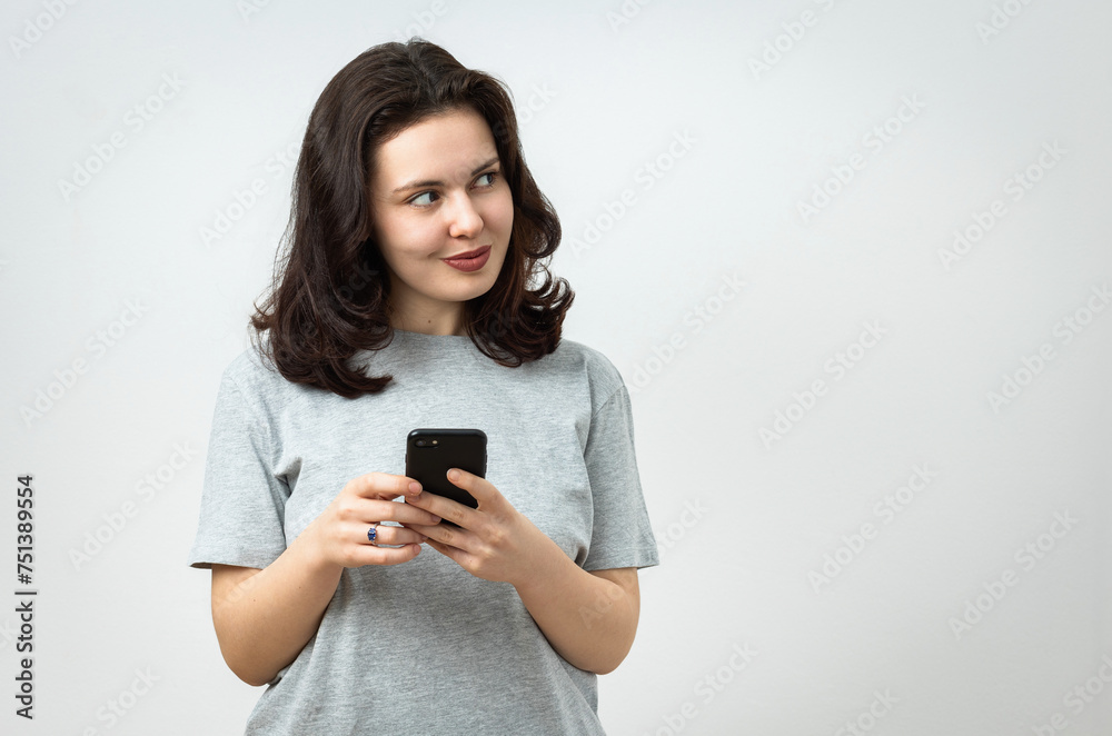 Cheerful beautiful young girl holding a cellphone and looking away, copy space, isolated on gray background Cheerful beautiful young girl holding a cellphone and looking away, copy space, isolated on gray background