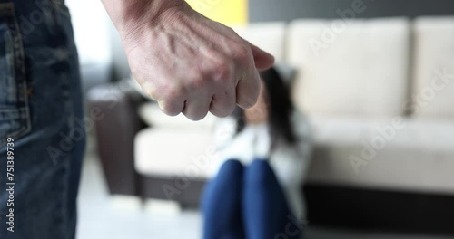 Man fist clenches in rage against the backdrop of frightened woman. Aggressive husband beating his abused wife, physical abuse and violence against a woman photo