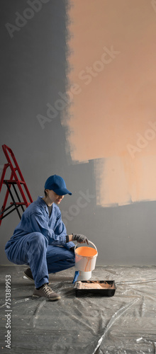 A painter pours orange paint from a bucket into a tray. The concept of repairing and painting walls in a house. Banner.