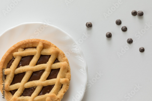 Mini crostata al cioccolato su piattino e tavolo bianco con gocce di cioccolato