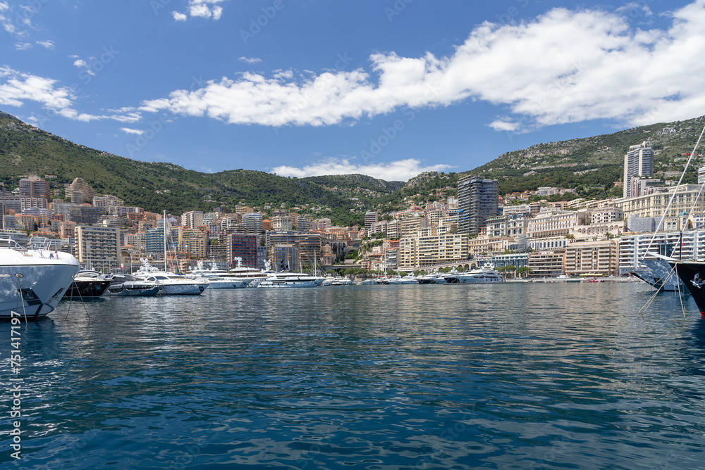 View of Monaco with its harbor and its many luxury yachts, its buildings and mountains in the background.