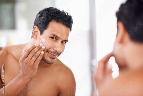 Skincare, mirror and cream with man in bathroom for morning routine, facial treatment and cosmetics. Self care, confidence and face of male person for sunscreen, lotion or moisturizer in reflection. photo