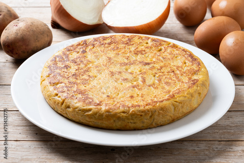 Traditional spanish omelette with ingredients on wooden table.