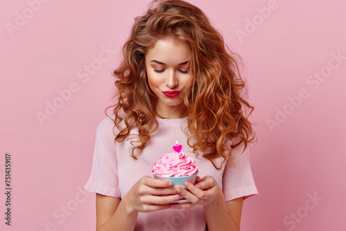Girl with cupcake in hands and burning candles, birthday on pink background