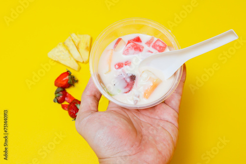 es buah or sup buah is indonesian fruit cocktail ice desert, contains strawberry, pineapple, and other tropical fruits mixed with ice cube, and condensed milk. isolated on yellow background. photo