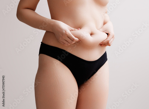 Fat woman hand holding fat belly on white background. A slightly overweight female figure in black sports underwear without a face close-up. Self acceptance and body positivity. unrecognizable