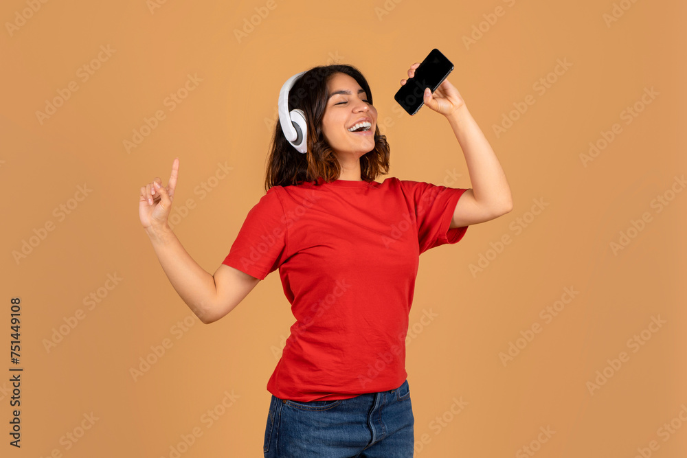 Happy young arabic woman singing karaoke on beige background Happy young arabic woman singing karaoke on beige background
