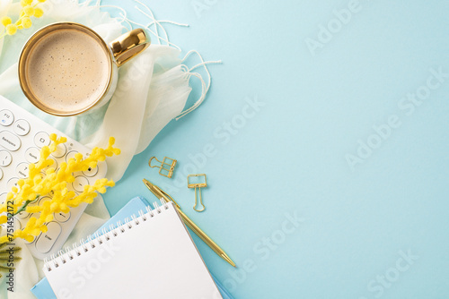 Spring's allure showcased in a top view of a bubbly americano, newly sprung mimosa, a streamlined keyboard, notepad, pen,clips, and a plush stole on a pastel blue base, space for words available photo
