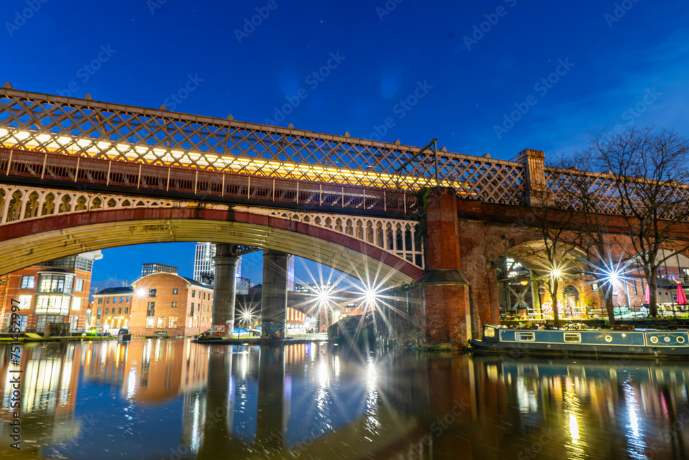 Long exposure night photo of a bridge and a tram driving over it at Castlefield, Manchester. 