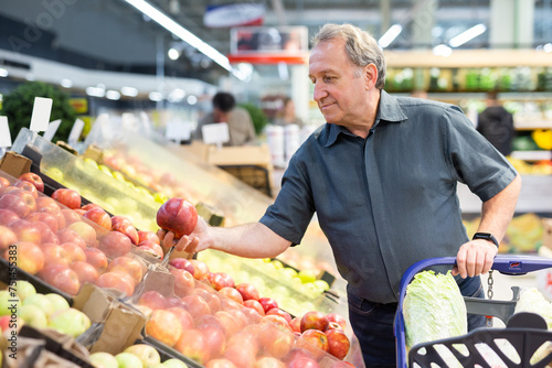 Satisfied man chooses ripe red apples on grocery store window
