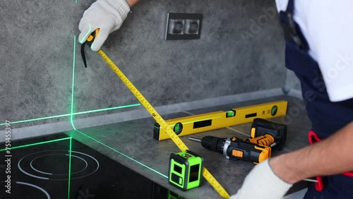 Man in uniform measures the level of the countertop with ruler and laser when assembling furniture.