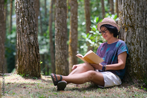 A woman is sitting under a tree while reading a book; serious expression photo