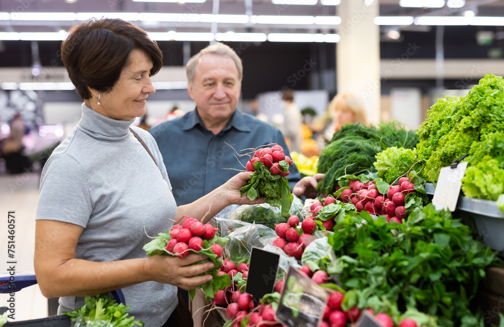 Elderly woman chooses radish in vegetable and fruit department