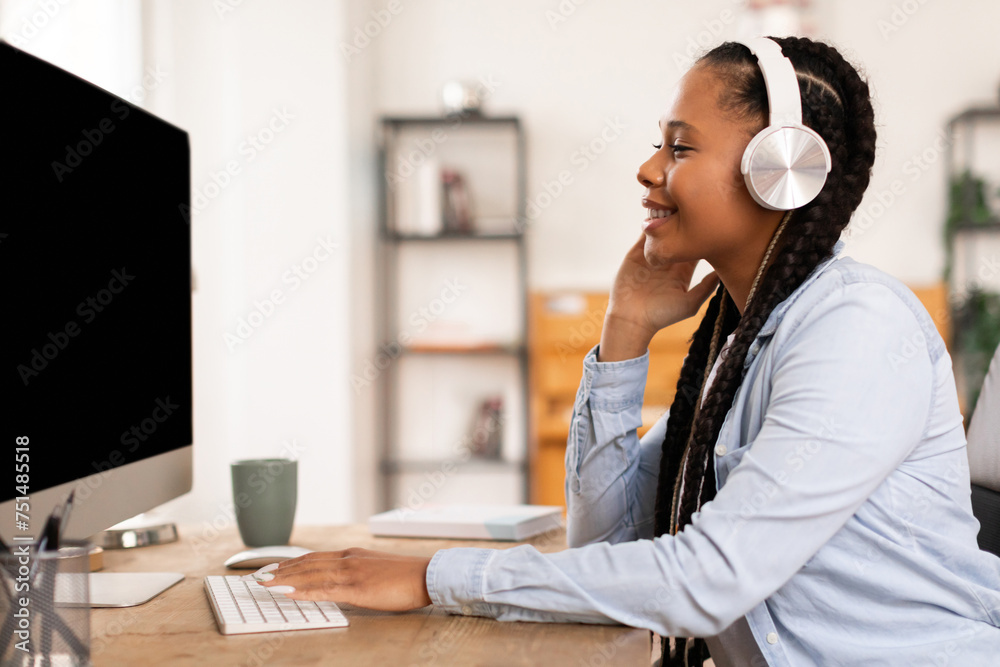 Focused black female teen studying online with headphones and computer - obrazy, fototapety, plakaty 