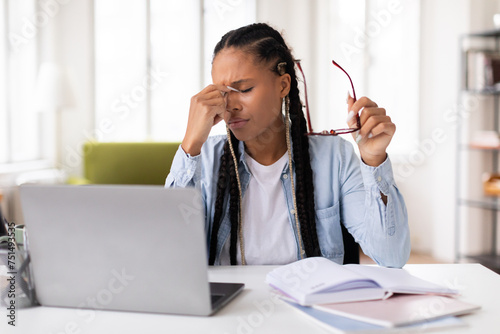 Stressed black lady student with headache studying at laptop photo