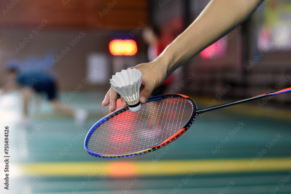 Badminton player holds racket and white cream shuttlecock in front of the net before serving it to another side of the court, soft focus.