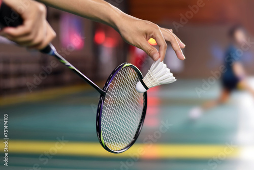 Badminton player holds racket and white cream shuttlecock in front of the net before serving it to another side of the court, soft focus.